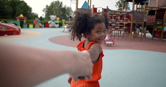 Pov shot of little afro girl holding mother hand walking on playground. Parent and afro-american daughter play together in park. Follow me concept