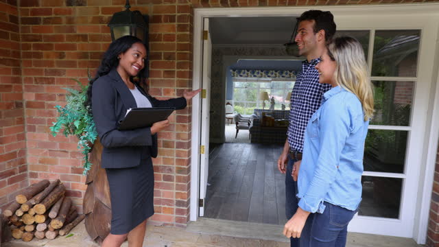 Happy real estate agent showing a house for sale to a Latin American couple looking very excited