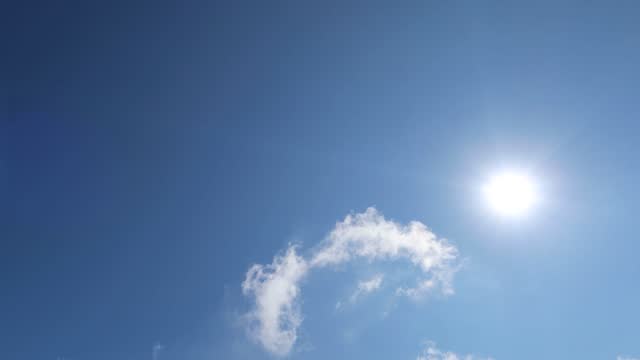 4k bright sun light ray and lens flare sunlight or sunbeam on dark deep blue clear sky with fluffy cumulus white clouds TimeLapse