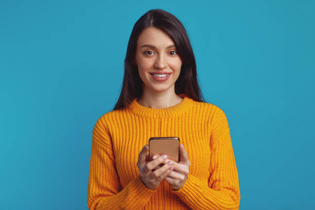 istock Young cute girl using smartphone while smiling against blue background 1500854973