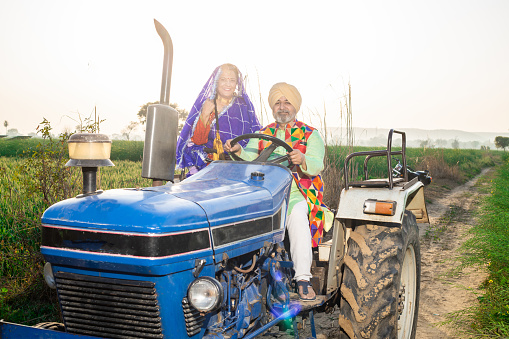 Happy senior punjabi sikh couple driving tractor at agriculture field outdoor. Rural india.