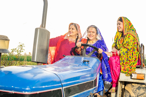 Group of happy punjab women driving tractor at agriculture field outdoor. Rural india.