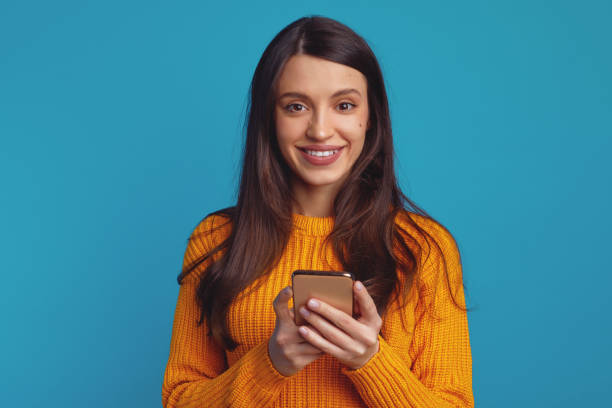 istock Young cute girl using smartphone while smiling against blue background 1500856052