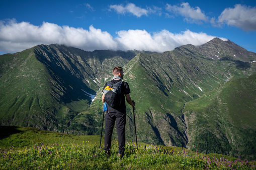 Rear view of hiker standing alone in the mountains and looking on beautiful mountain range against him