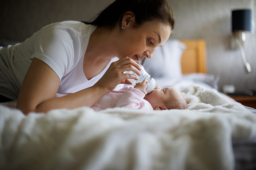 Smiling mother feeding her newborn baby girl with bottle at home
