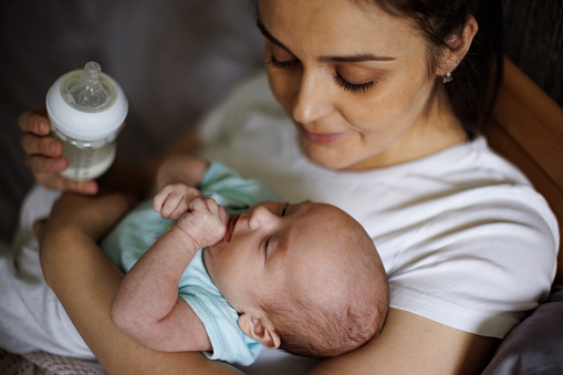 Mother feeding her newborn baby with bottle at home