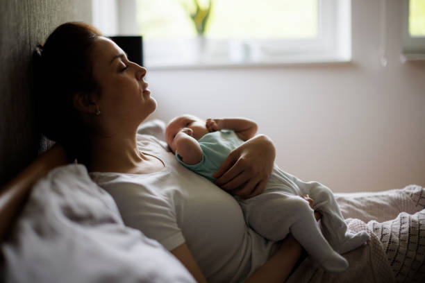 Tired mother lying in bed with her newborn baby stock photo