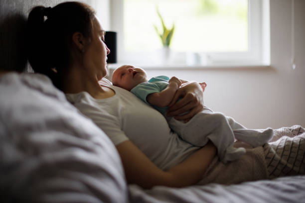 Tired mother lying in bed with her newborn baby stock photo