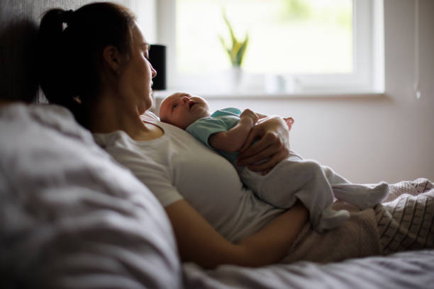 Tired mother lying in bed with her newborn baby - fotografia de stock