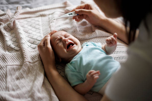 Mother checking body temperature of her crying baby with a thermometer stock photo