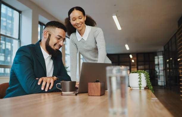 istock A young businesswoman is standing and pointing at her laptop computer while a young businessman sits and looks with copy space. Stock photo 1500858844
