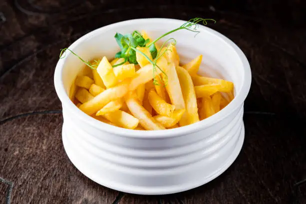 Photo of Salted French fries in white bowl on a wooden table