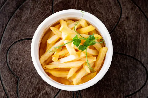 Photo of Salted French fries in white bowl on a wooden table