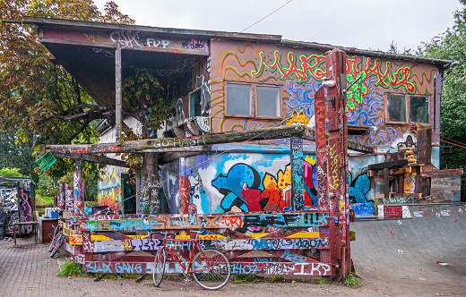 Copenhagen, Denmark - September 14, 2010: Christiania freetown. Colorful graffiti cacophony on walls, pillars and everything. Green foliage and gray sky. Red bike present