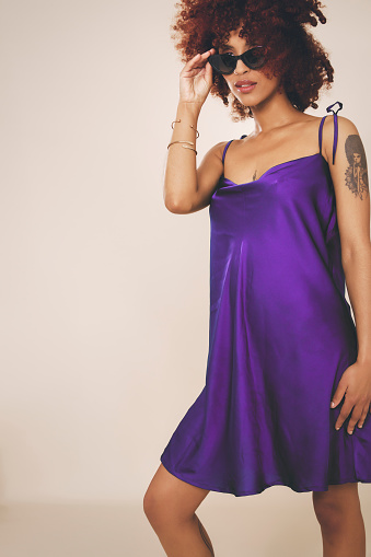 Beautiful woman wearing a stylish purple dress and smiling against a beige background.