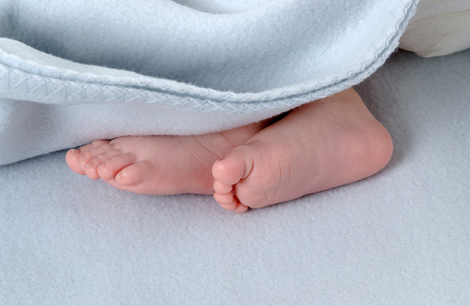 Pair of small newborn baby feet close up under a blanket in bed