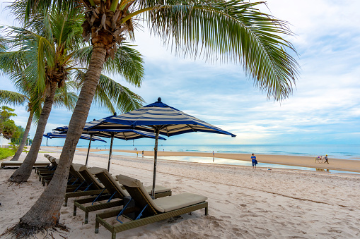 Sun chairs and parasol under a palm tree at a tropical beach, Hua Hin, Prachuap Khiri Khan, Thailand, Jun 19, 2023.