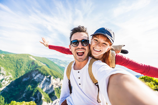 Happy couple taking a selfie hiking mountains - Successful hikers on the top of the peak cliff smiling at camera - Young man and woman enjoyng in summer holiday - Travel, nature, hike, sport concept
