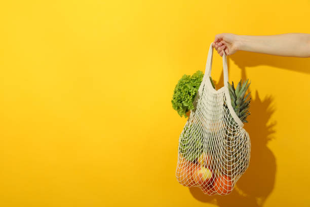 istock Female hand holds string bag with food on yellow background 1500886155