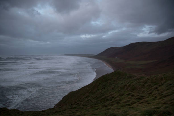 Rhossili Bay during a winter's storm Rhossili Bay at dusk during a winter's storm with dramatic skies, wind and rain. Rhossili Downs are covered with bracken and waves are pounding the beach at high tide. rhossili bay stock pictures, royalty-free photos & images