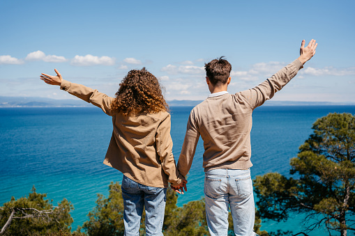 Young couple with hands raised towards sky enjoying the beautiful view.