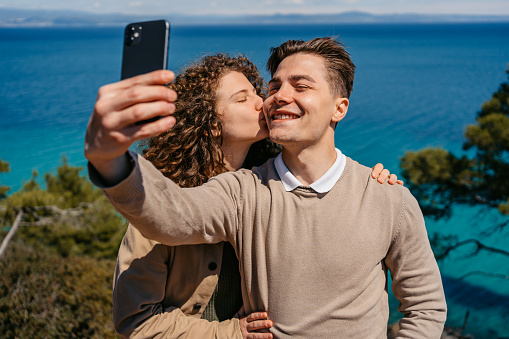 Beautiful young couple taking selfies on the coast in Greece.