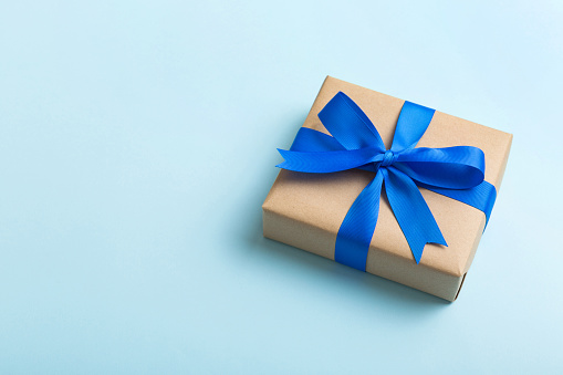 Realistic 3D render of a blue gift box tied with blue ribbon.  Gift box is isolated on white background. Clipping path for gift box and ribbon is included. Side view. Horizontal composition with copy space.