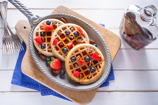 Traditional belgian homemade waffles with blueberry, honey and orange jam on metal grid on light background.