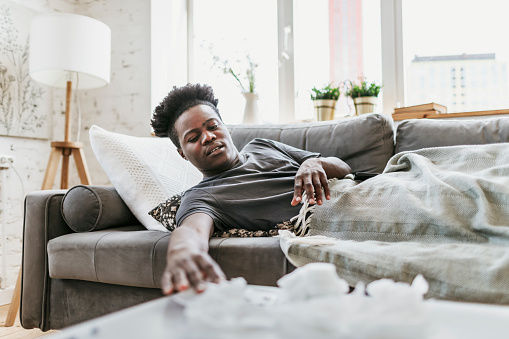 Young adult black man lying down at home with a flu and runny nose