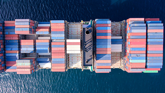 Aerial top view of a fully loaded container ship in the open sea.