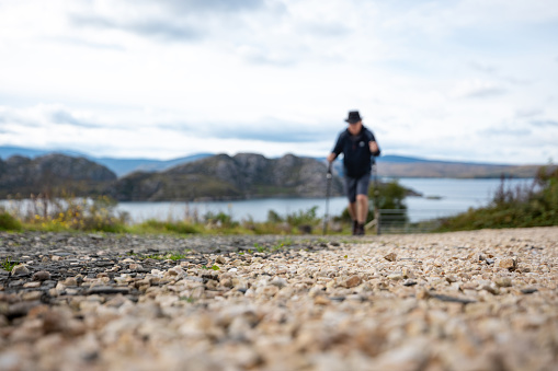 A low angle selective focus wide angle view of an unrecognisable male hiker who is is on a hike in the Scottish highlands in Loch Torridon he is using hiking poles for the multi terrain walk.