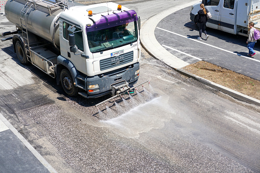 Truck is washing and cleaning and cooling street during preparations for adding a new asphalt while the pedestrians are walking by. High angle view. Ljubljana, Slovenia, Europe.