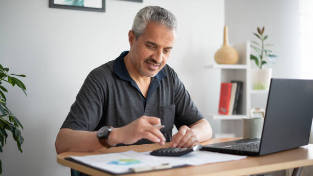 istock Smiling adult man using calculator while working at home 1500910127