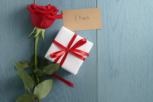 red rose on blue wood table with gift box and 8 march day paper card, with copy space