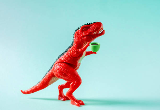 istock Red toy dinosaur holding cup of coffee on blue background. 1500917015
