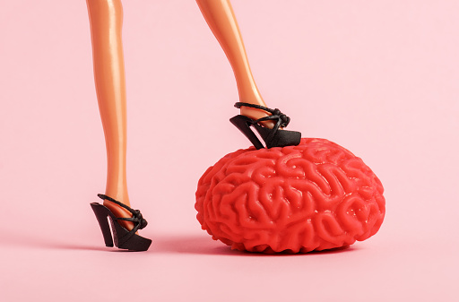 Female feet trample the human brain model on a pink background. Hack the brain concept.