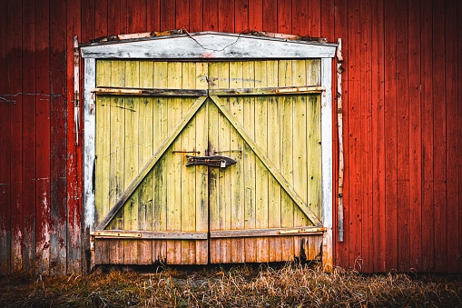 A pair of large dirty yellow wooden doors on a wooden red barn
