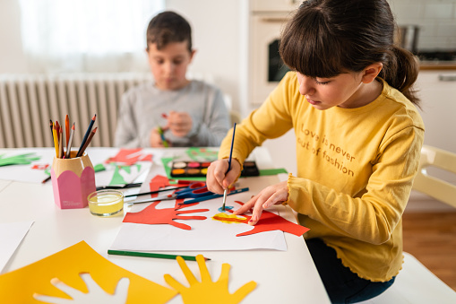 Creative children doing crafting, making human hands with colorful paper at home