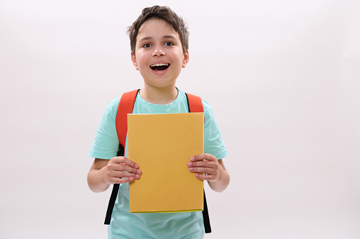 Caucasian emotional happy teenage school boy holds textbooks, smiles looking at camera, standing over white isolated background. Copy advertising space. Back to school on new semester of academic year