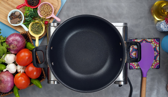Cooking pan along with different vegs and hotplate on grey mat
