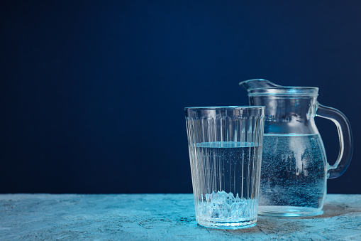 Jug and glass of water on blue textured background