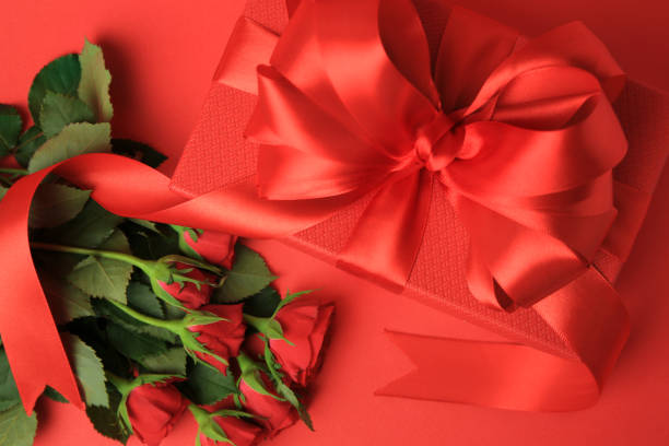 istock Beautiful gift box with bow and roses on red background, flat lay 1500946574