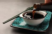 Pouring soy sauce into bowl on grey table, closeup