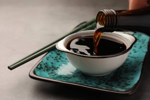 Pouring soy sauce into bowl on grey table, closeup Pouring soy sauce into bowl on grey table, closeup soia sauce stock pictures, royalty-free photos & images