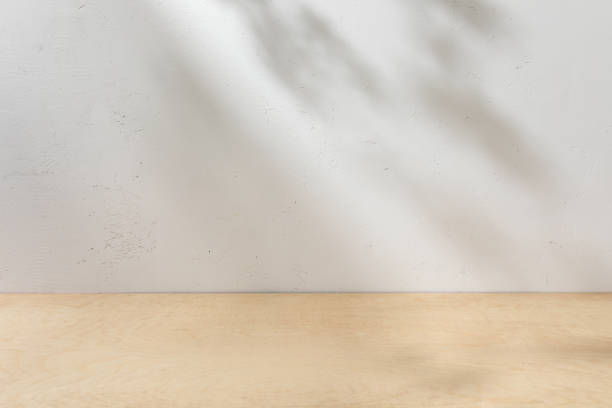 istock Wooden table mockup on a stucco background with tree branch shadows on the wall. Mock up branded products and displays. 1500955672