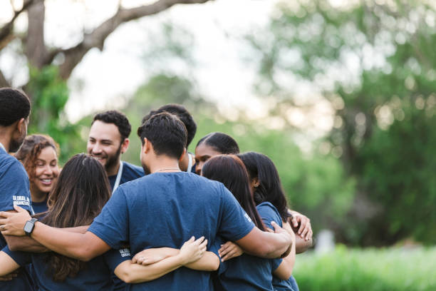 Diverse group stands in huddle to review day After working together all day, the multiracial group stands with their arms around each other in a huddle to review their accomplishment. community outreach stock pictures, royalty-free photos & images