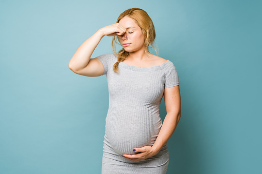 Young pregnant woman in a studio pinching her nose and looking disgusted by some smells during pregnancy