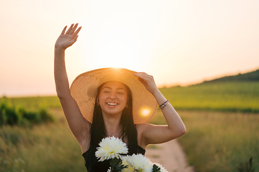 Beautiful girl with a hat enjoying summer day riding a bike. She is waving to someone.