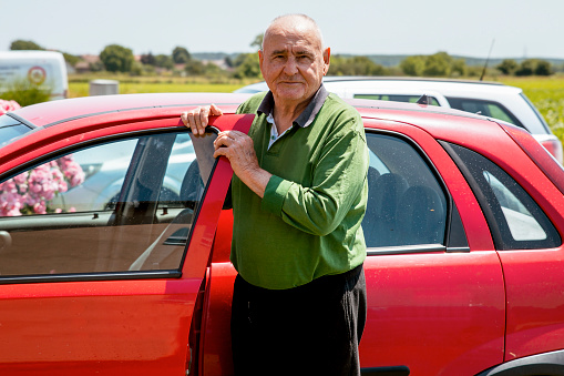 Senior man satisfied about his new red car. Elderly male driver going on a road trip. Copy space