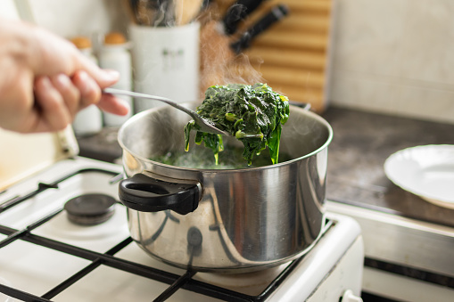 hand cooking boiled chard and spinach in a steaming pot on the stove